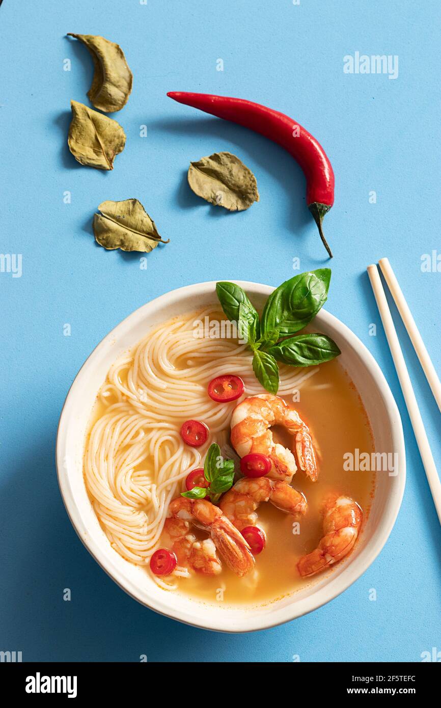 Tom Yum Suppe in Schüssel mit Essstäbchen auf blauem Hintergrund Stockfoto