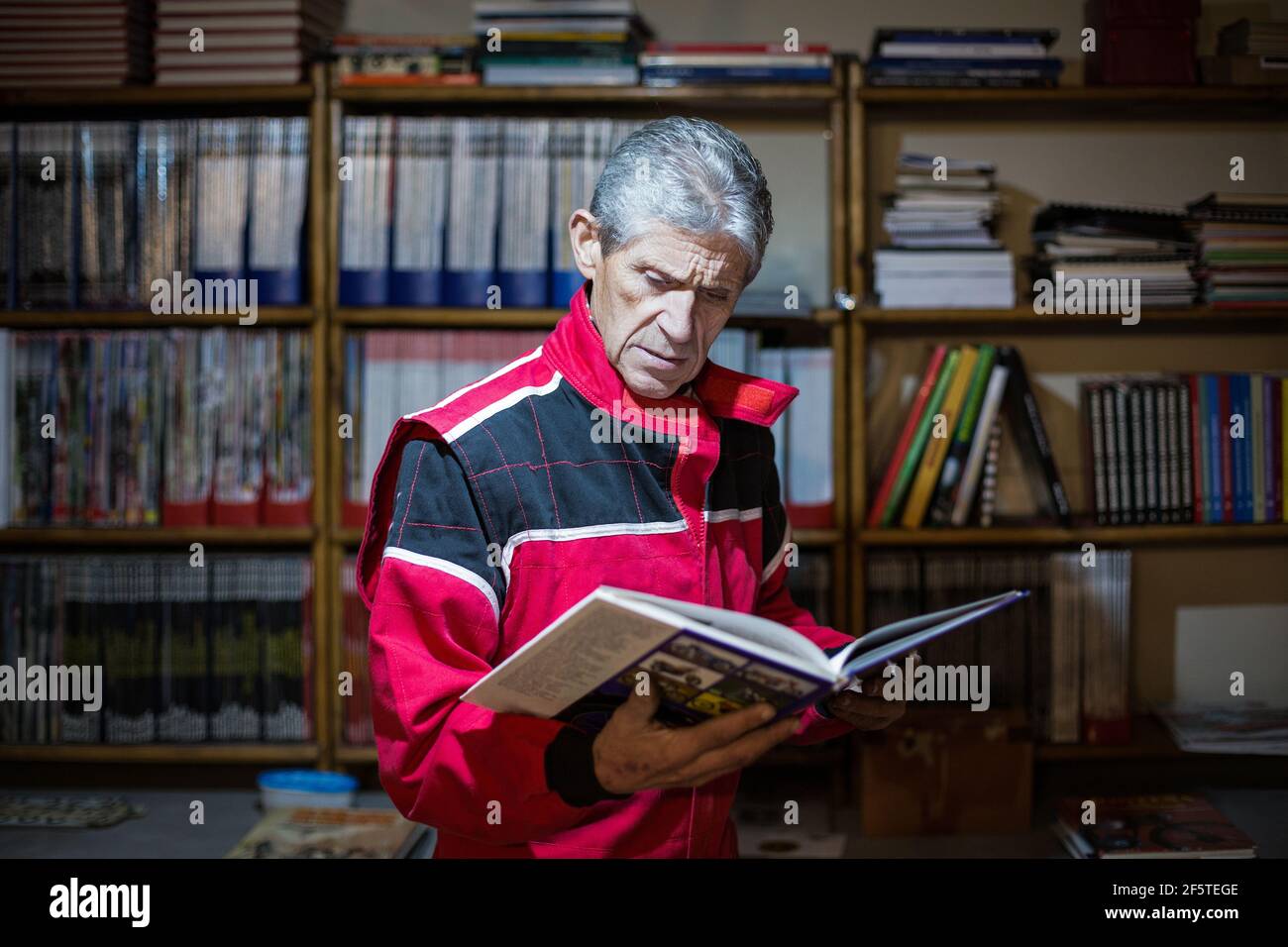 Fokussierte Senior männlichen Mechaniker in Arbeitskleidung Lesen professionelle Buch, während Suche nach Lösung des technischen Problems in der Nähe von Bücherregal Stockfoto