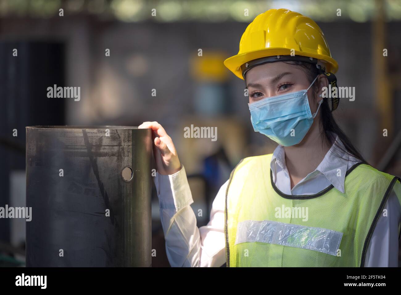 Ein Porträt einer Ingenieurin mit Maske, die in einer Fabrik steht. Arbeiten im Konzept der Produktionsanlage für die Schwerindustrie. Stockfoto