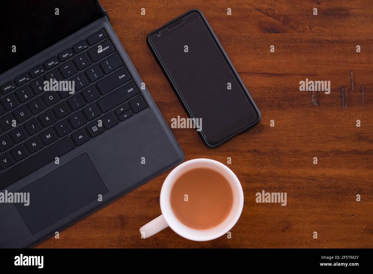 Laptop-Tastatur mit Smartphone und einer Tasse Kaffee/Tee auf einem rustikalen Holztisch. Moderne Büroflächen. Mobiles Büro. Arbeiten Sie von zu Hause oder von überall aus. Stockfoto