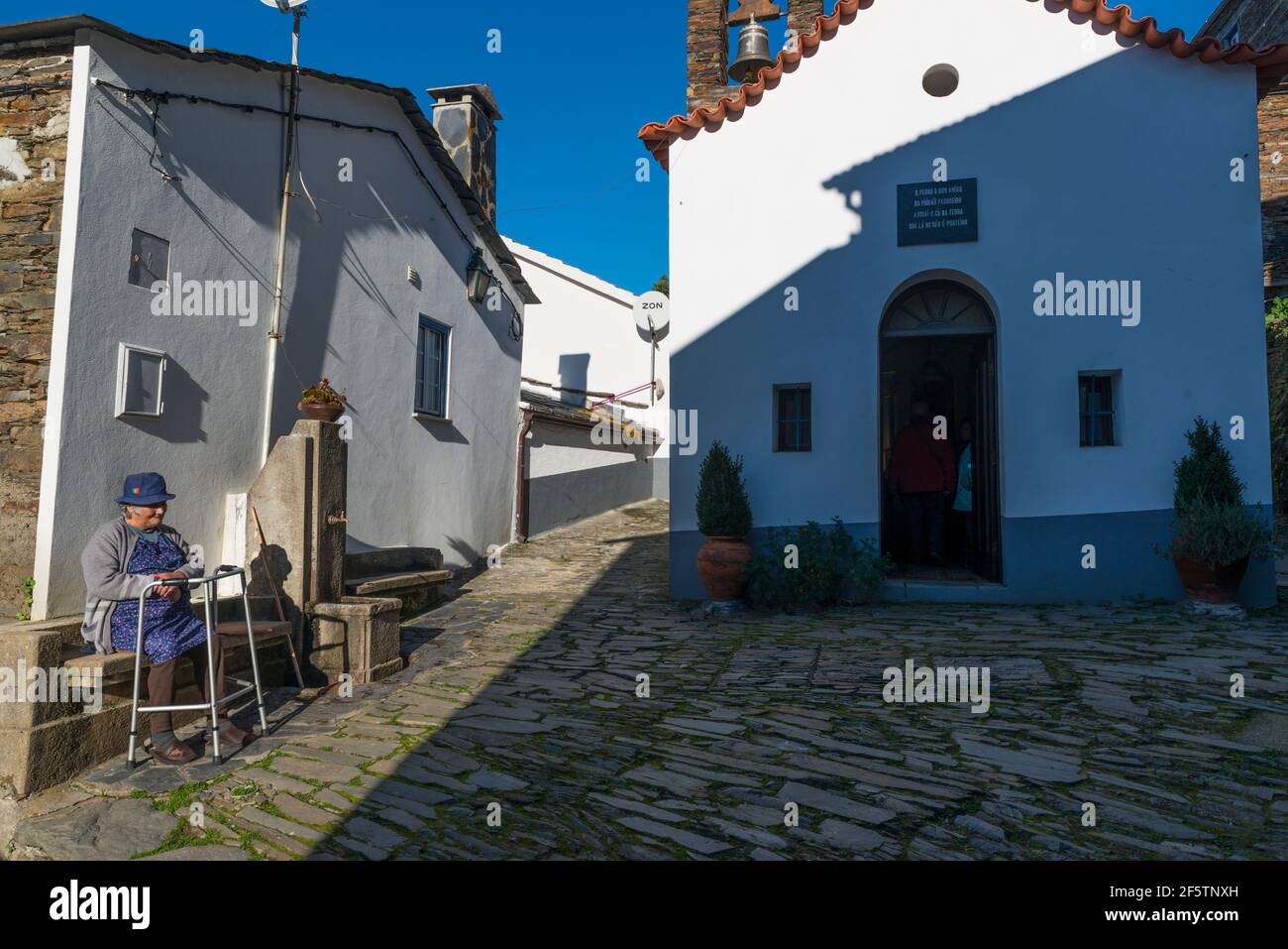 Alte Dorfbewohnerin mit Spaziergängern, die sich in dem kleinen traditionellen Dorf Piodao, Portugal, ausruhen. Stockfoto