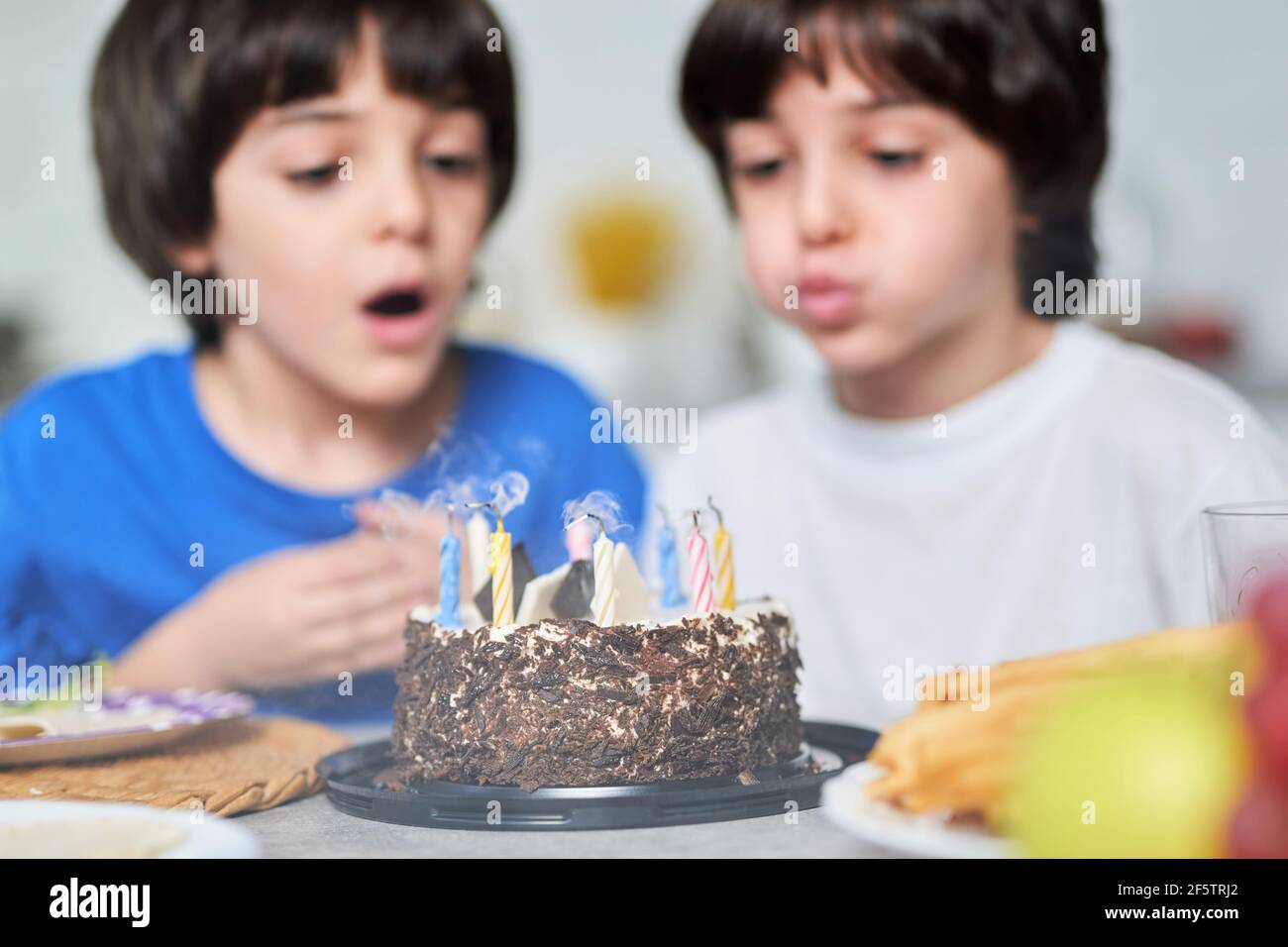 Geburtstagsjungen. Zwei kleine lateinische Jungen blasen Kerzen auf einem Geburtstagskuchen, während sie zusammen mit der Familie zu Hause Geburtstag feiern Stockfoto