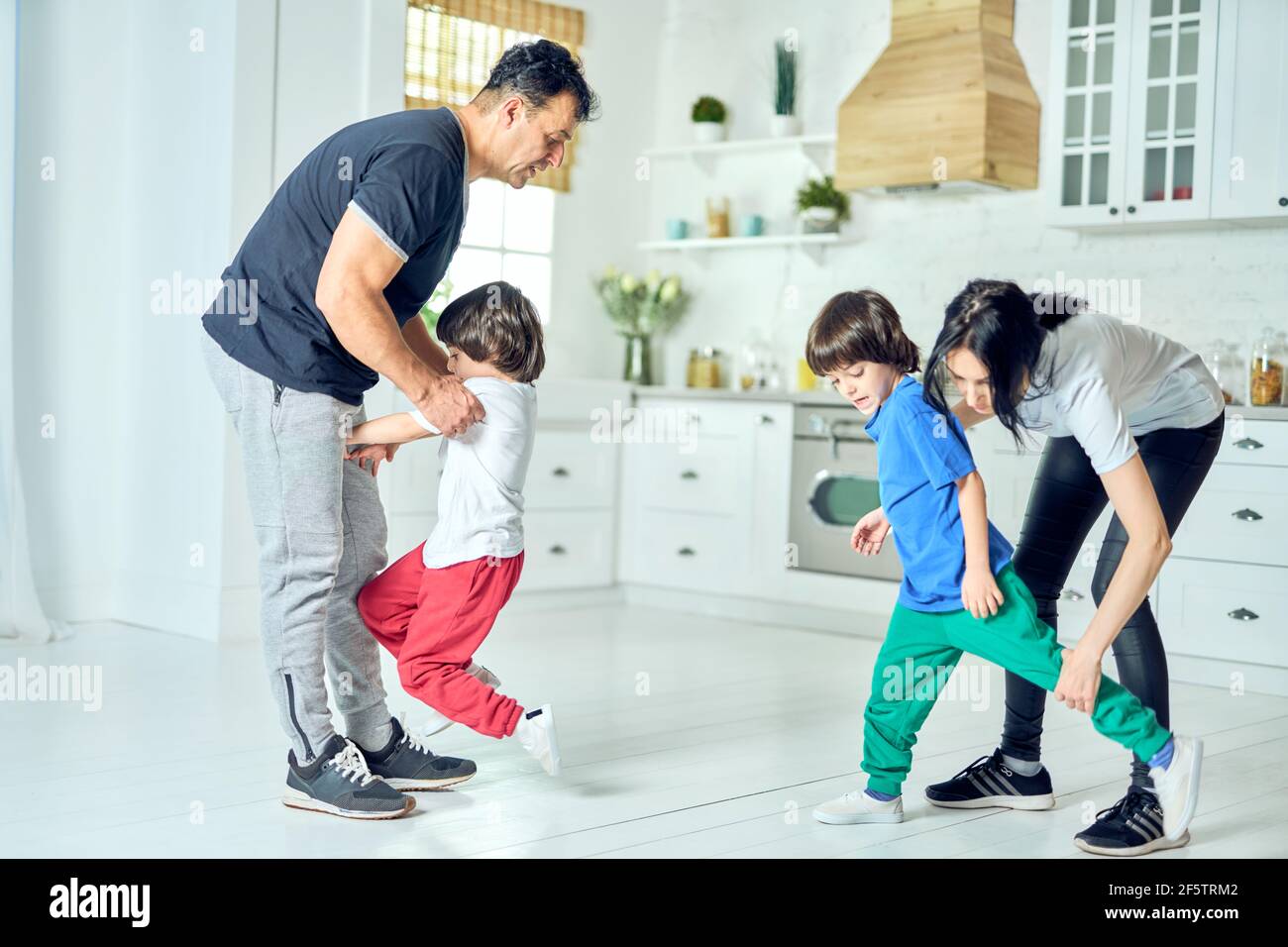 Aktive lateinische Eltern mittleren Alters, die zwei kleine Jungen machen Übungen am Morgen zu Hause. Gesunder Lebensstil Stockfoto