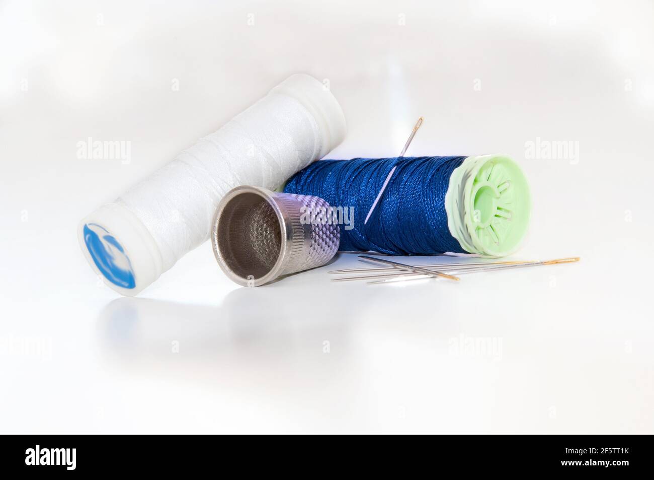 Nahaufnahme der weißen und blauen Fadenspulen mit Nadeln Und Nähzeug auf einem hellen weißen Hintergrund Stockfoto
