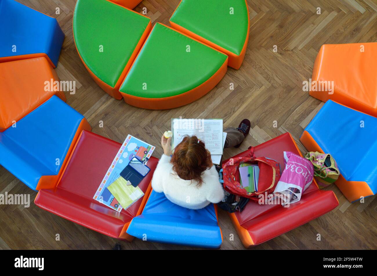 Junge Frau, die in der Lounge-Zone der öffentlichen Bibliothek sitzt und die Zeitschrift liest. Stockfoto