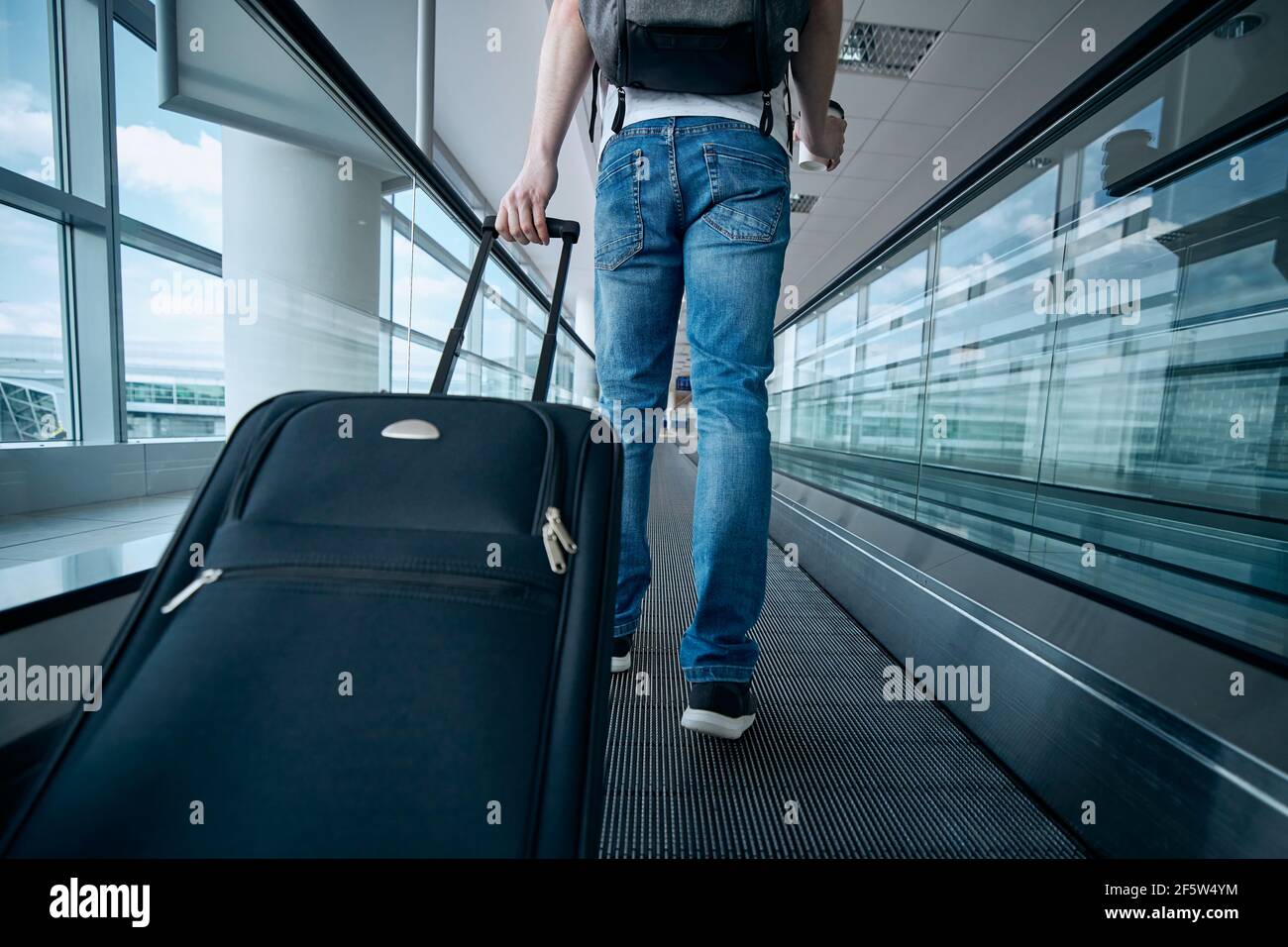Mann, der mit dem Koffer läuft. Rückansicht des Reisenden auf dem beweglichen Gang am Flughafenterminal. Stockfoto
