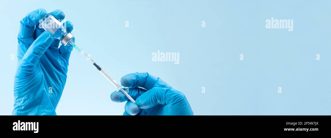 Behandeltes Arzt Hände füllen Fläschchen Spritze auf blauem Hintergrund in Bannerformat mit Kopierbereich Stockfoto
