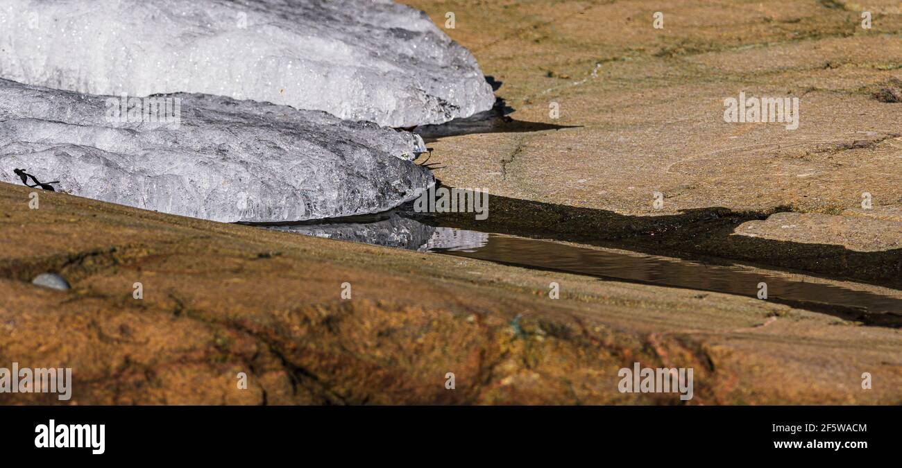 Warmes Frühlings Sonnenlicht schmelzendes Eis bildet kleinen Bach über Felsen Stockfoto