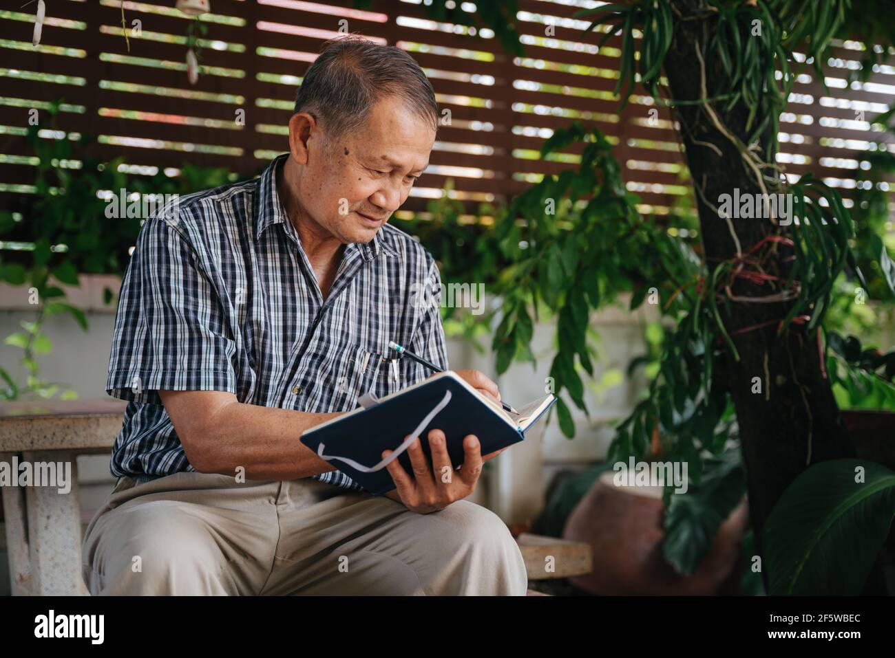 Senior thai Mann sitzt auf Marmorstuhl unter dem Baum und schreiben Sie Notizen, Alzheimer-Krankheit Konzept. Stockfoto