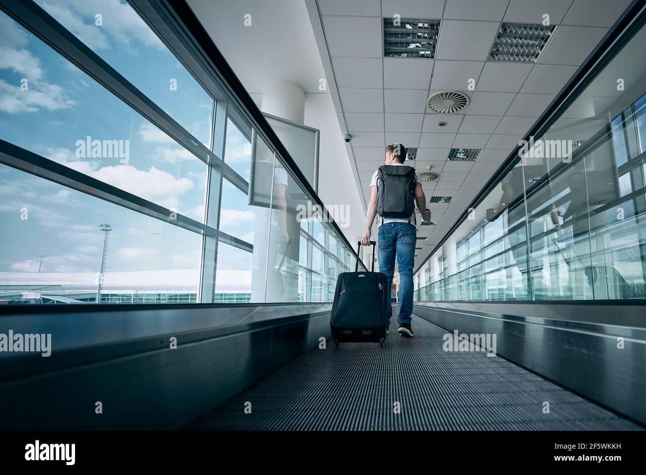 Mann, der mit dem Koffer läuft. Rückansicht des Reisenden auf dem beweglichen Gang am Flughafenterminal. Stockfoto
