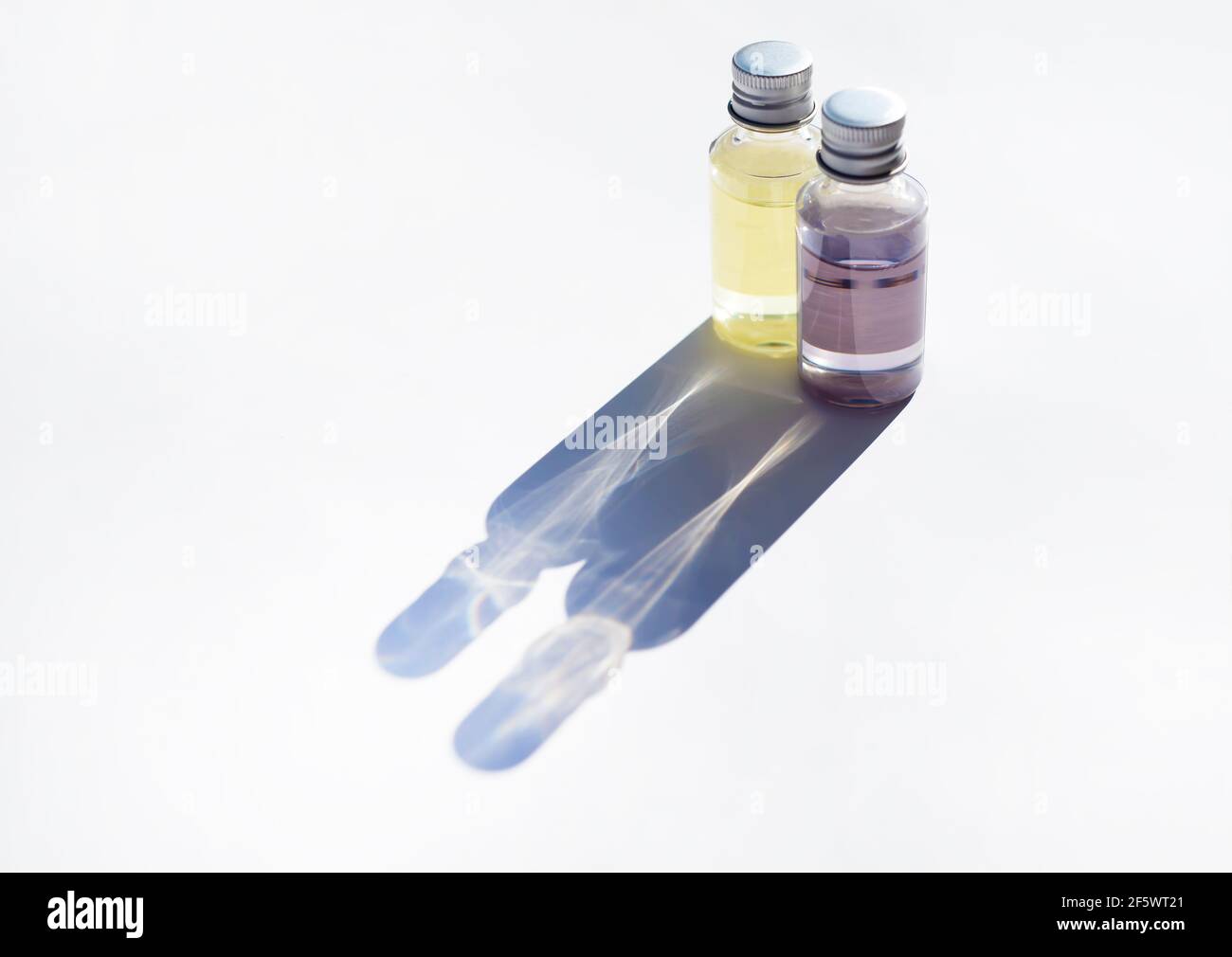 Zwei Parfümflaschen und eine Reflexion von ihnen. Duftendes Öl in transparenten Gläsern. Durchbrochene Schatten. Stockfoto