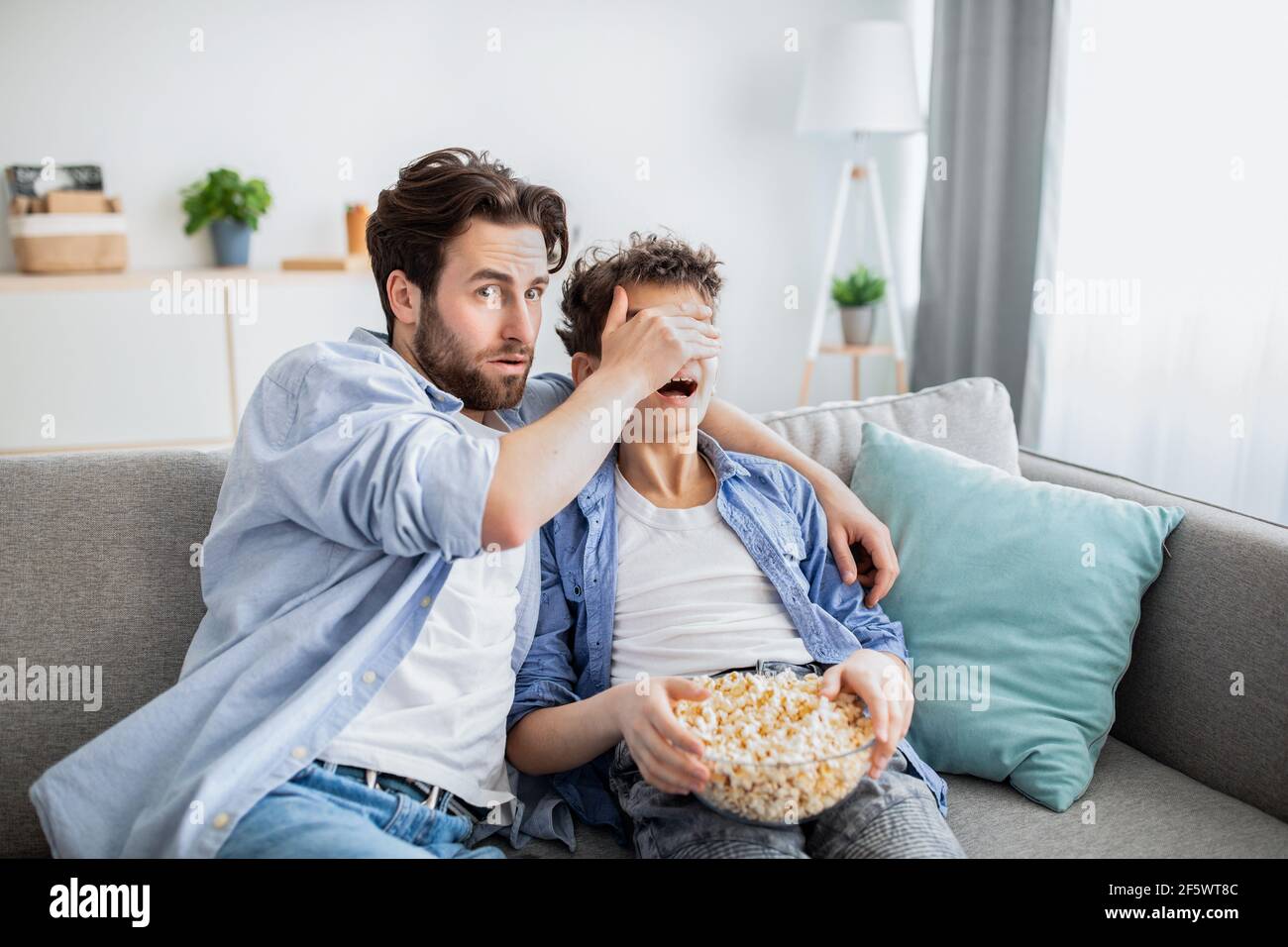 Vater verdeckt die Augen seines Sohnes vor unangemessenen Inhalten, während er zuschaut Film im fernsehen mit Popcorn Stockfoto