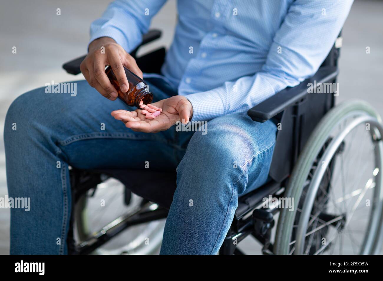 Selbstmord bei Menschen mit Behinderung. Behinderter junger Mann, der eine Handvoll Pillen aus dem Glas gießt, Nahaufnahme Stockfoto