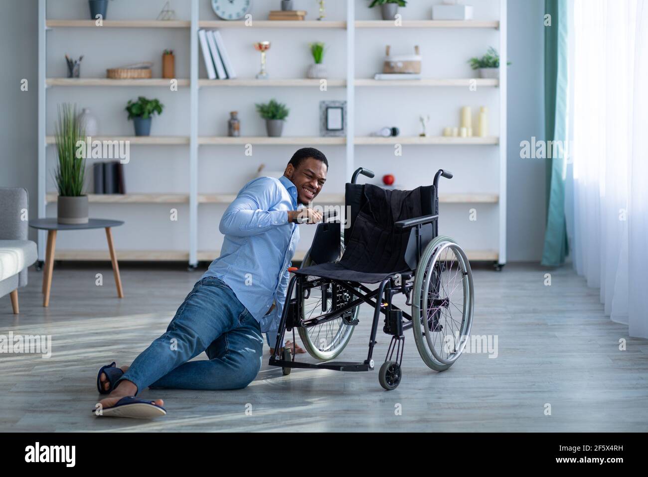 Junger schwarzer Mann mit Behinderung liegt auf dem Boden nach dem Sturz Unten vom Rollstuhl zu Hause Stockfoto