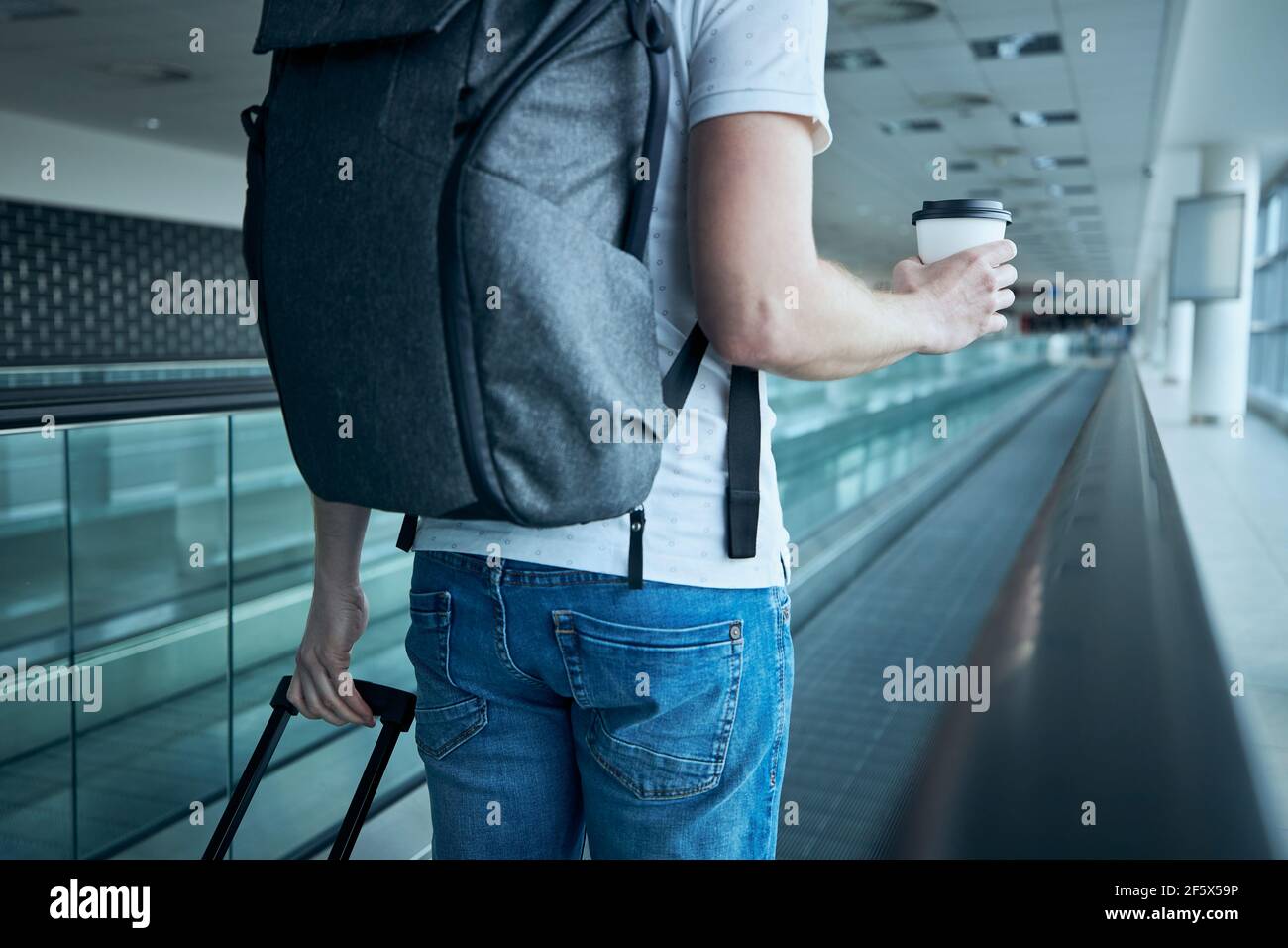 Mann, der mit Papierkaffeetasse läuft. Reisende auf einem beweglichen Gang am Flughafenterminal. Stockfoto