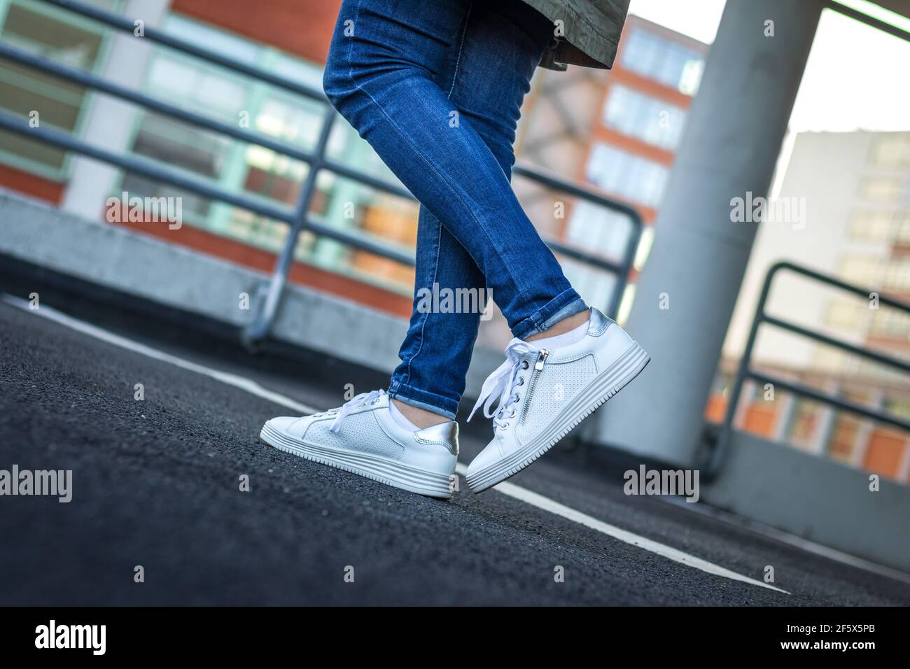 Frau mit weißen Turnschuhen in der Stadt. Weibliche Beine tragen Jeans und Leder-Sportschuh. Stadtleben. Modekonzept Stockfoto