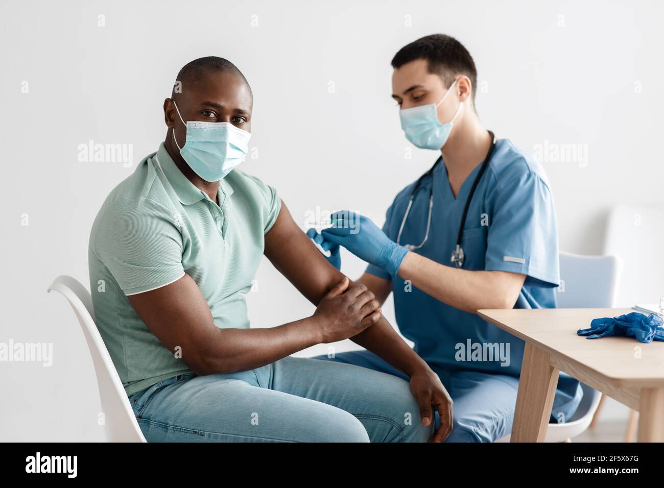Krankenschwester in medizinischen Gesichtsmaske und Handschuhe halten Spritze und geben an Patienten Grippe, covid-19 Injektion in Arm Stockfoto