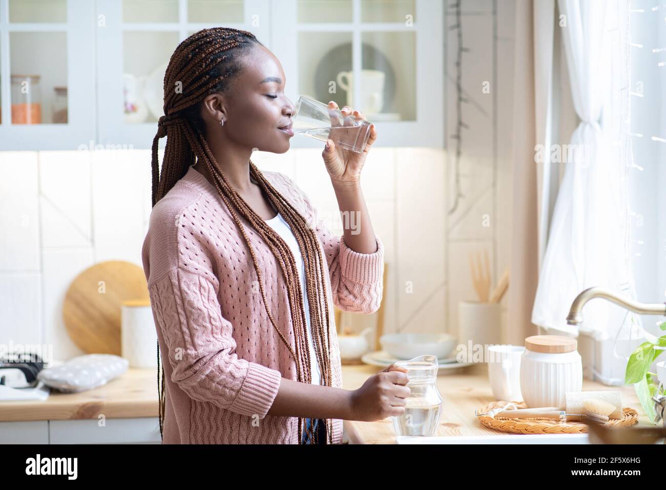Durstige Afroamerikanische Frau Trinkwasser Aus Glas In Der Küche Zu Hause Stockfoto