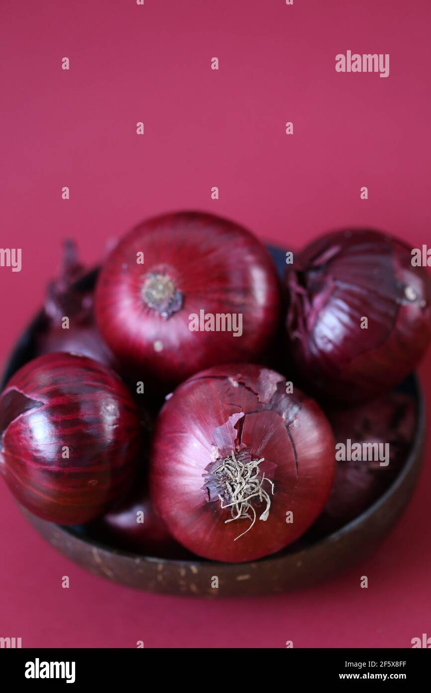 Rote Zwiebel auf einem hellen burgundigen Hintergrund.Frische Bio-Bio-Gemüse auf dem Bauernhof.Lebensmittelzutat.Rote Zwiebel in einer braunen Tasse gesetzt. Stockfoto