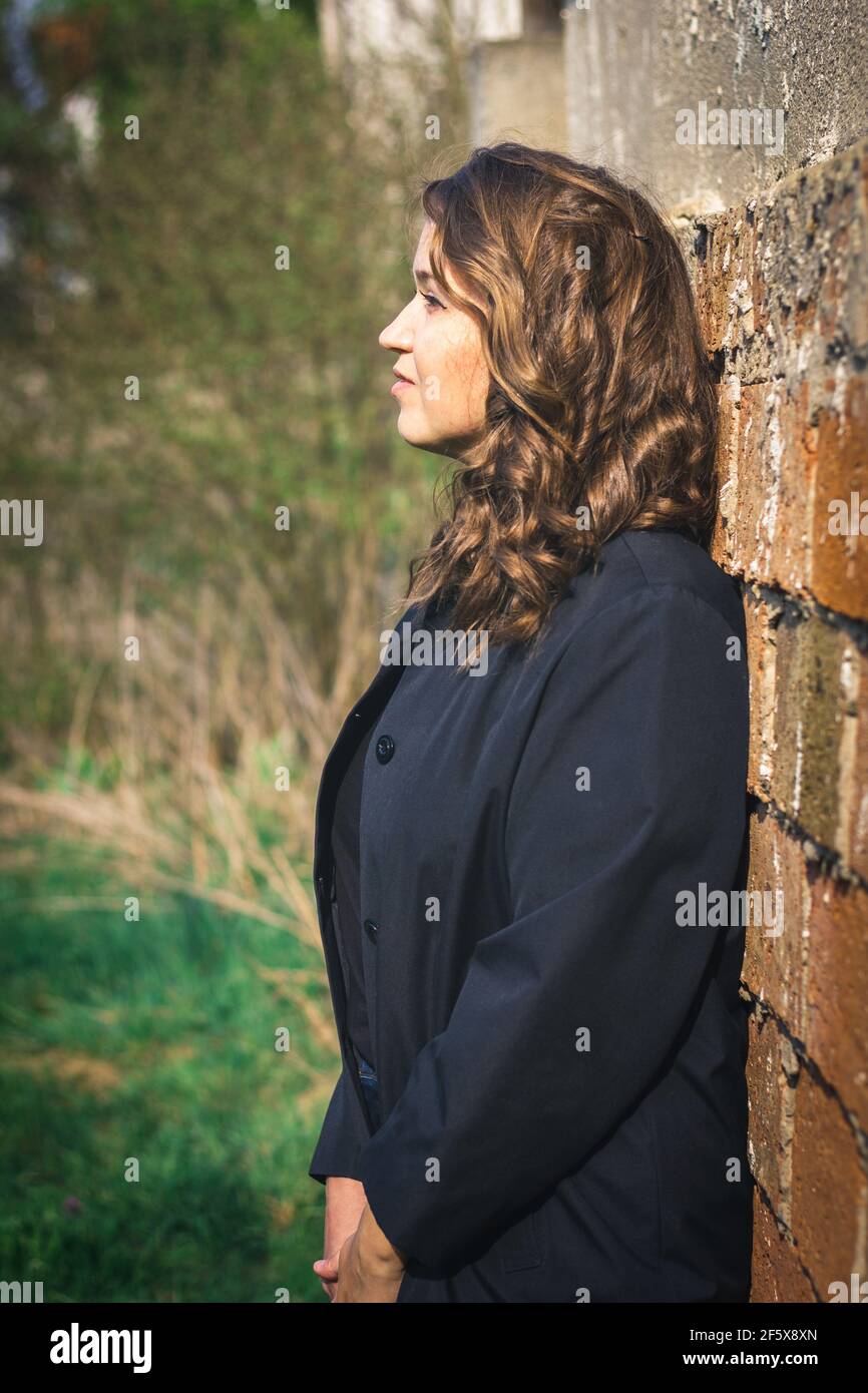 Portrait von schönen braunen Haaren junge Frau lehnte Wand. Stilvolle kaukasische Frau trägt schwarze Jacke Stockfoto