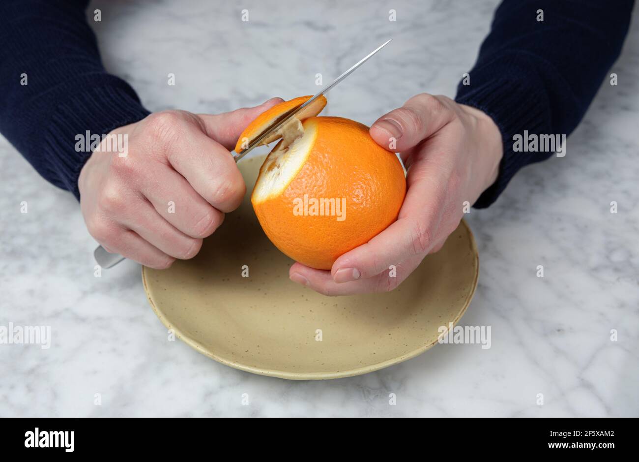 Männerhände schälen eine Orange mit einem Messer. Gesunde Ernährung Konzept Stockfoto