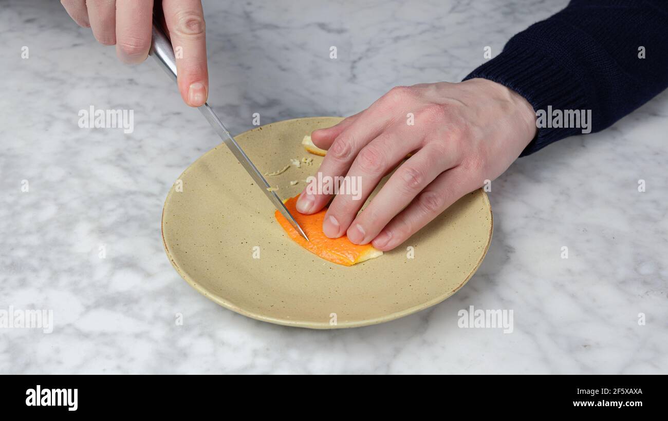 Die Hand eines Mannes, der mit einem Messer die Haut einer Orange schneidet. Falsche Zähne Stockfoto