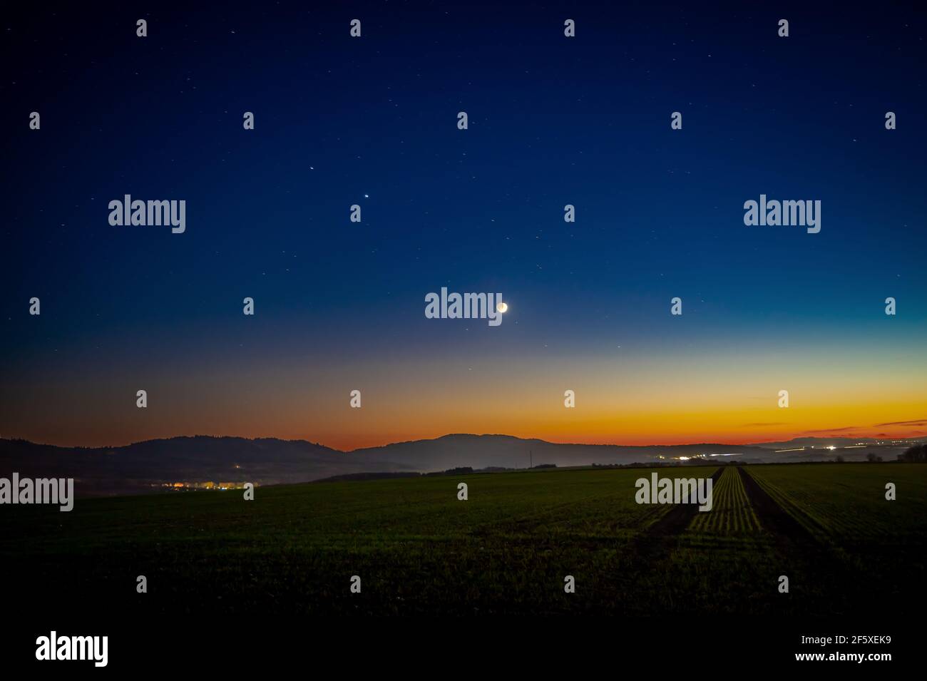 Eine schöne Aufnahme von aufsteigendem Saturn, Jupiter und Mond über der Wiese nach Sonnenuntergang Stockfoto