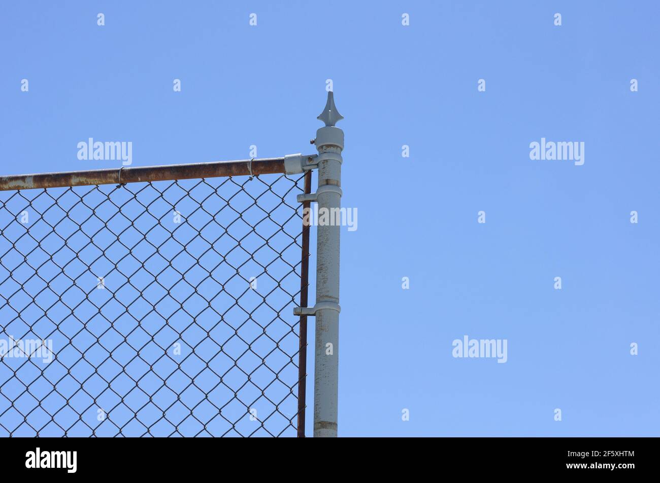 Kettengliedzaun und Endpfosten mit Speer gegen Ein strahlend blauer Himmel Stockfoto