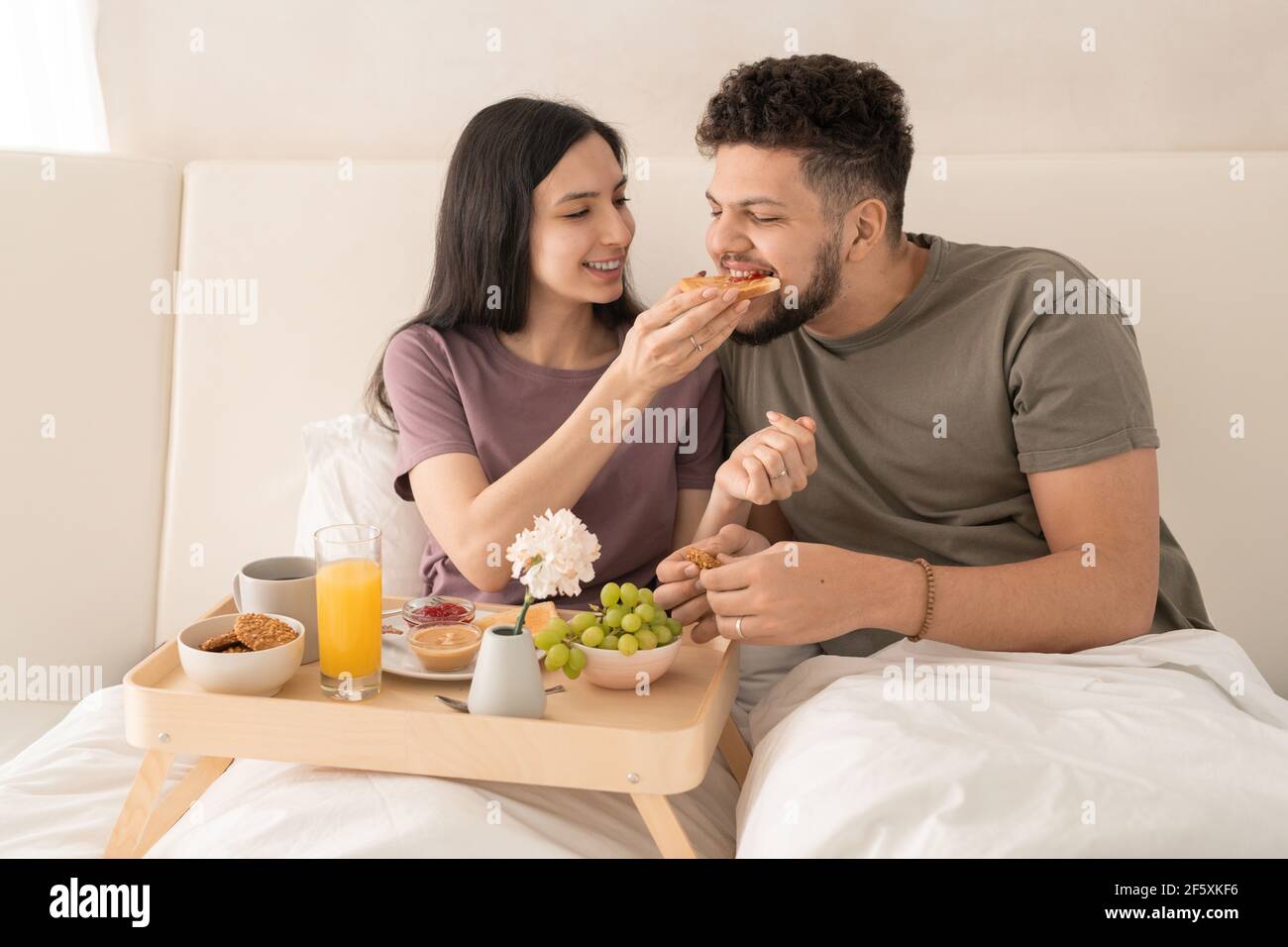 Junge fröhliche Frau, die Sandwich mit Marmelade in ihren Mann Mund ...