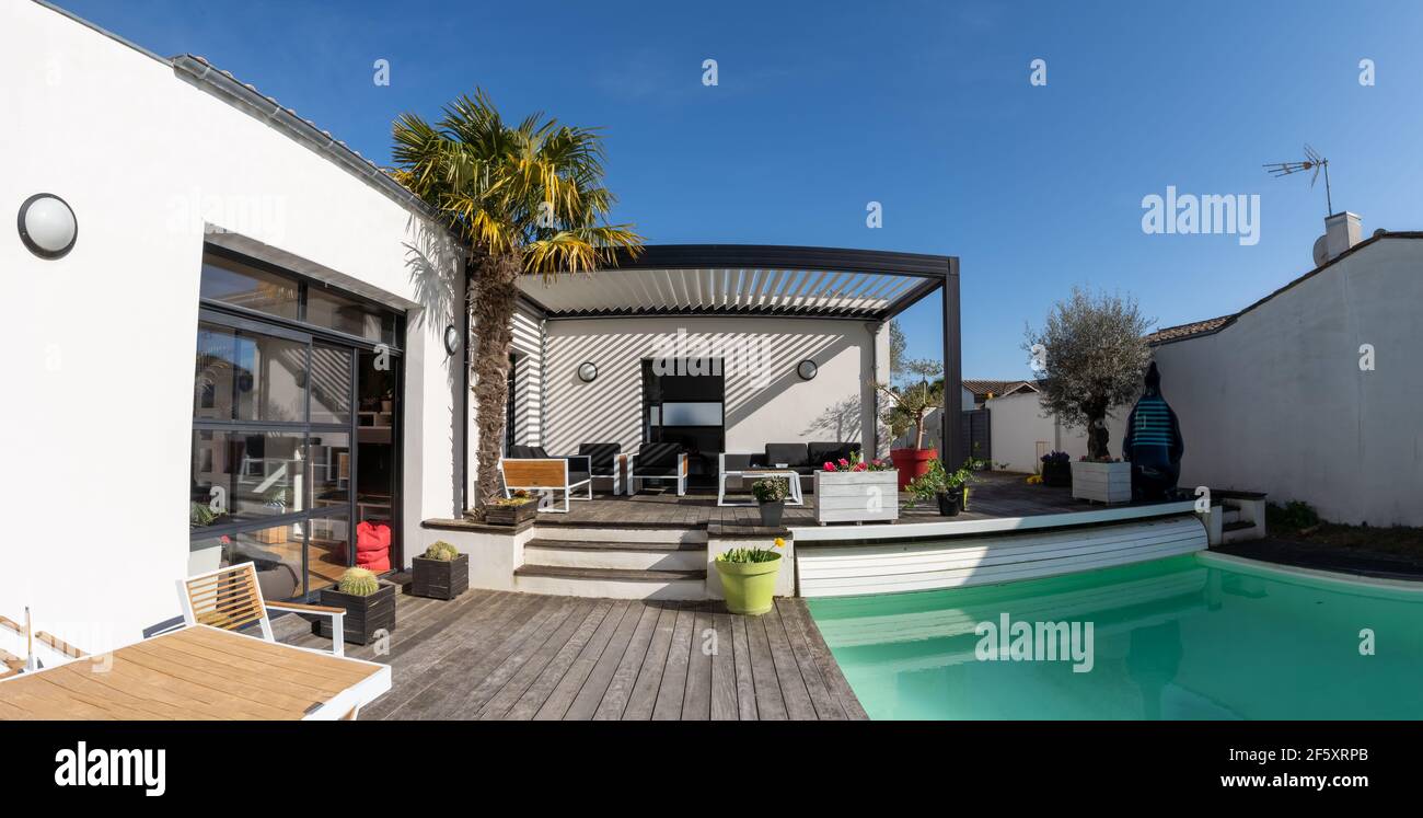 Trendige Outdoor modernes Haus, Markise und Terrassendach, Gartenlounge, Stühle, Metallgrill umgeben von Landschaftsgestaltung Stockfoto