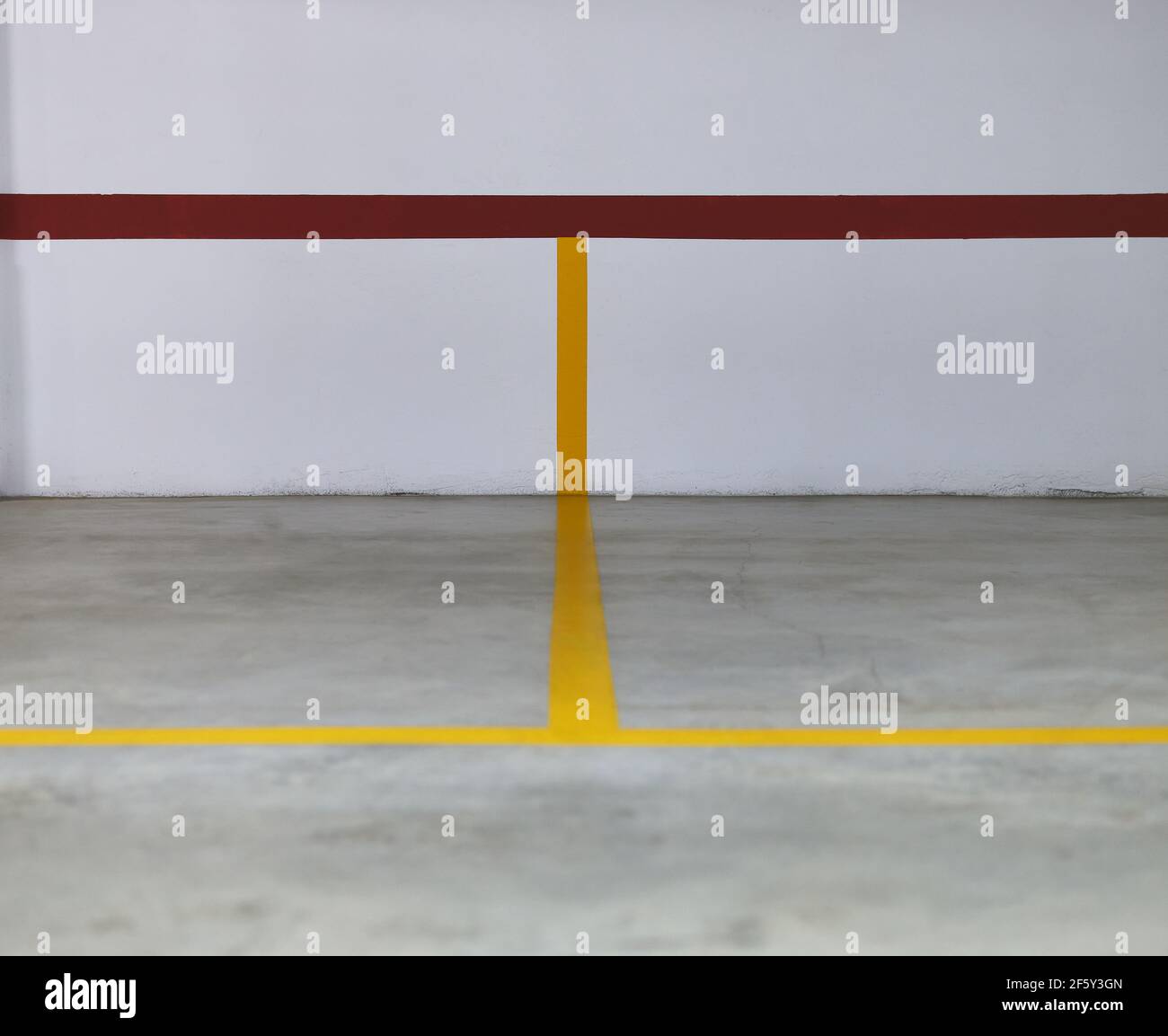 Detail einiger gelber und roter Linien an einer Wand Und ein Betonboden, der einige Parkplätze begrenzt Stockfoto