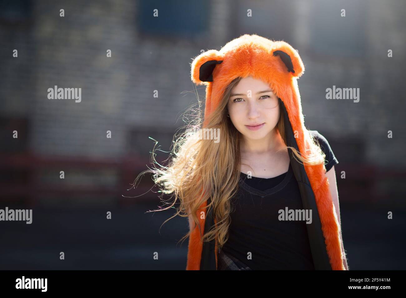 Teen Mädchen mit langen Haaren in orange Geist Kapuze, hinterleuchtet, in der Stadt. Stockfoto