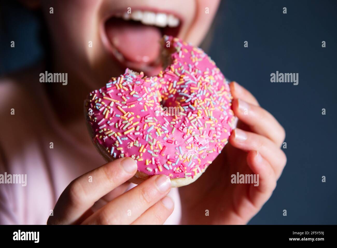 Lächelndes Mädchen mit Mund offen essen rosa donat auf einem Dunkler Hintergrund Stockfoto