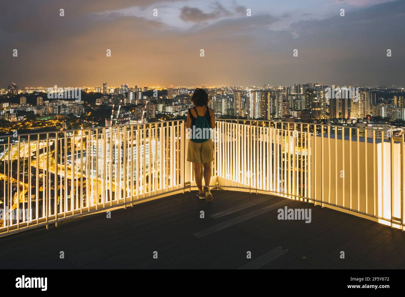 Junge Frau, die in der Abenddämmerung den Blick auf die Innenstadt von Singapur von einem Dach aus genießt. Stockfoto