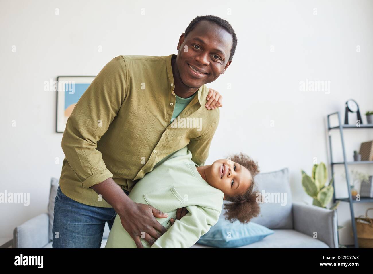 Porträt eines glücklichen afroamerikanischen Vaters, der mit seiner Tochter zu Hause spielt und die Kamera anlächelt, den Kopierraum Stockfoto