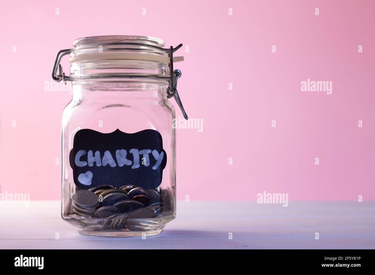 Glas mit Münzen mit Kreideanhänger Charity auf rosa Hintergrund. Spenden- und Wohltätigkeitskonzept. Speicherplatz kopieren. Stockfoto