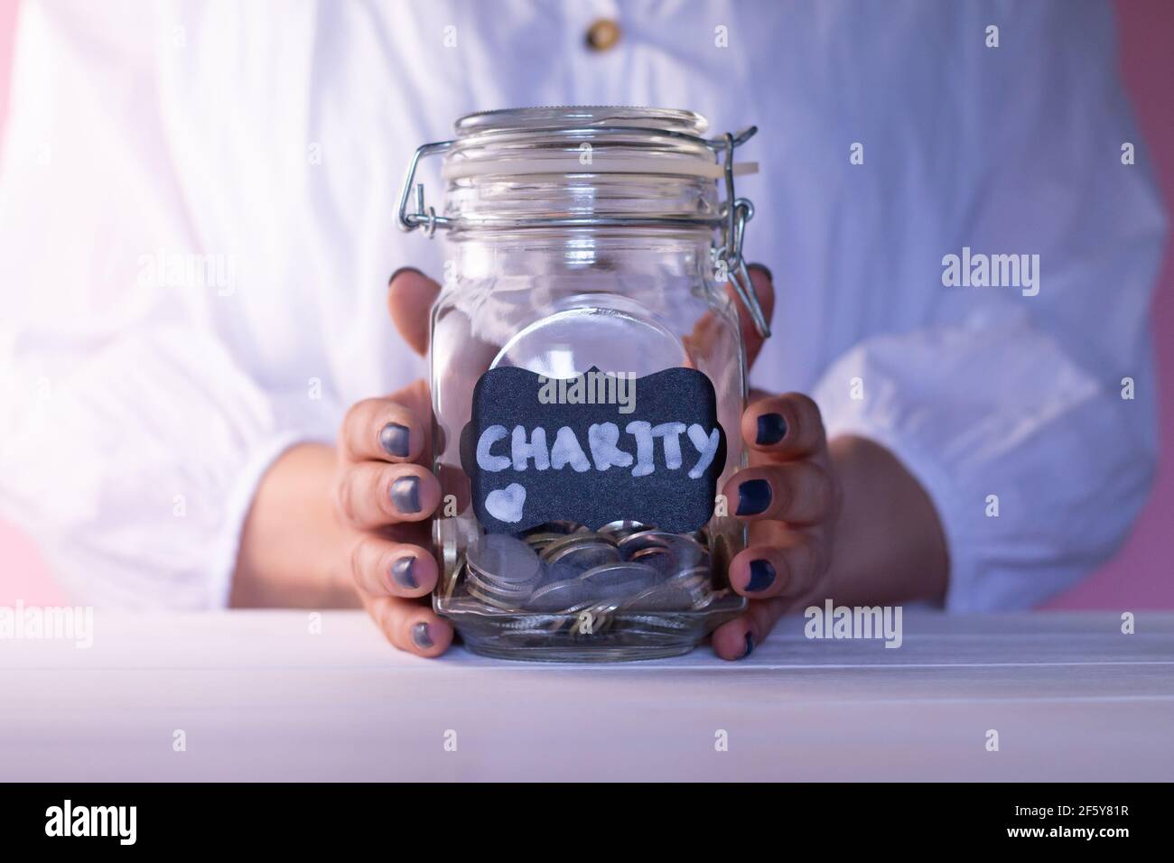 Frau Hände halten ein Glas mit Münzen mit einer Kreide Charity-Tag. Spenden- und Wohltätigkeitskonzept Stockfoto