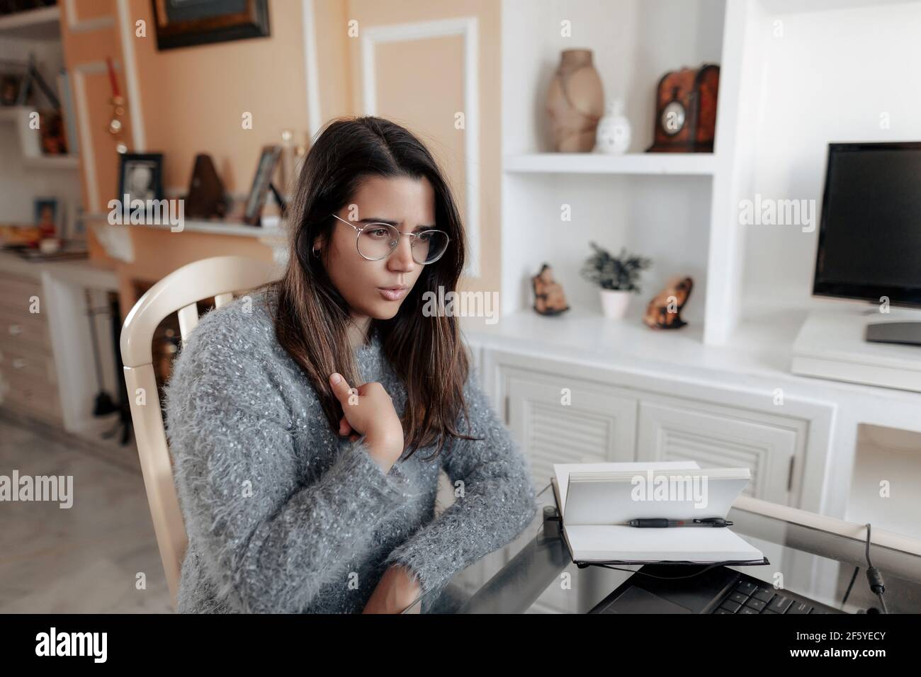 Medium shot junge taube Frau trägt eine Brille und ein Pullover ist mit Gebärdensprache Namen buchstabieren, während in einem Online-Videoanruf in ihrem Wohnzimmer. Stockfoto