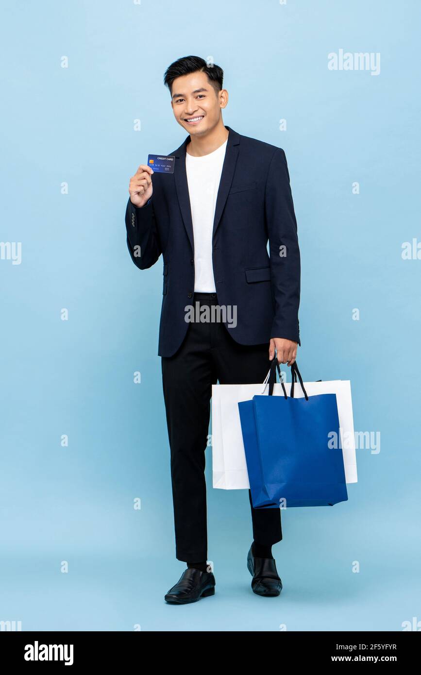 Schöner südostasiatischer Mann mit Einkaufstasche und Kreditkarte Für bargeldloses Zahlungskonzept in isoliertem Studio hellblauem Hintergrund Stockfoto