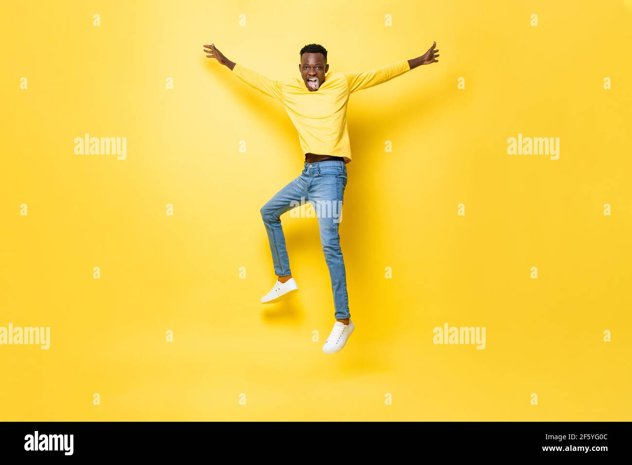 Junge fröhlich energischen afrikanischen Mann springen mit ausgestreckten Händen isoliert Auf gelbem Studiohintergrund Stockfoto