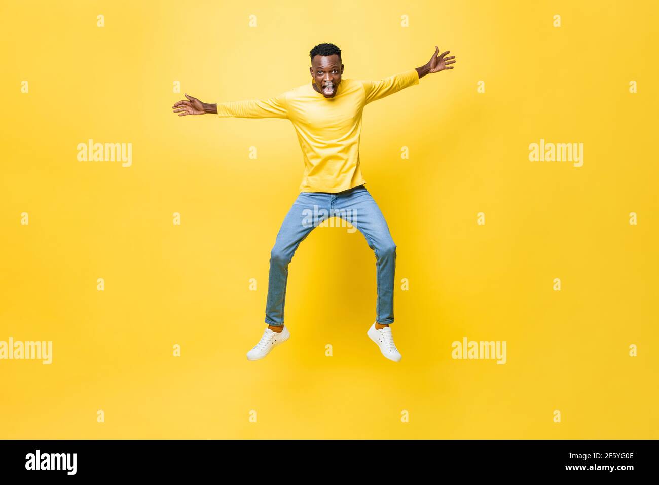 Junge aufgeregt afrikanischen Mann springen mit ausgestreckten Händen isoliert auf Gelber Studiohintergrund Stockfoto