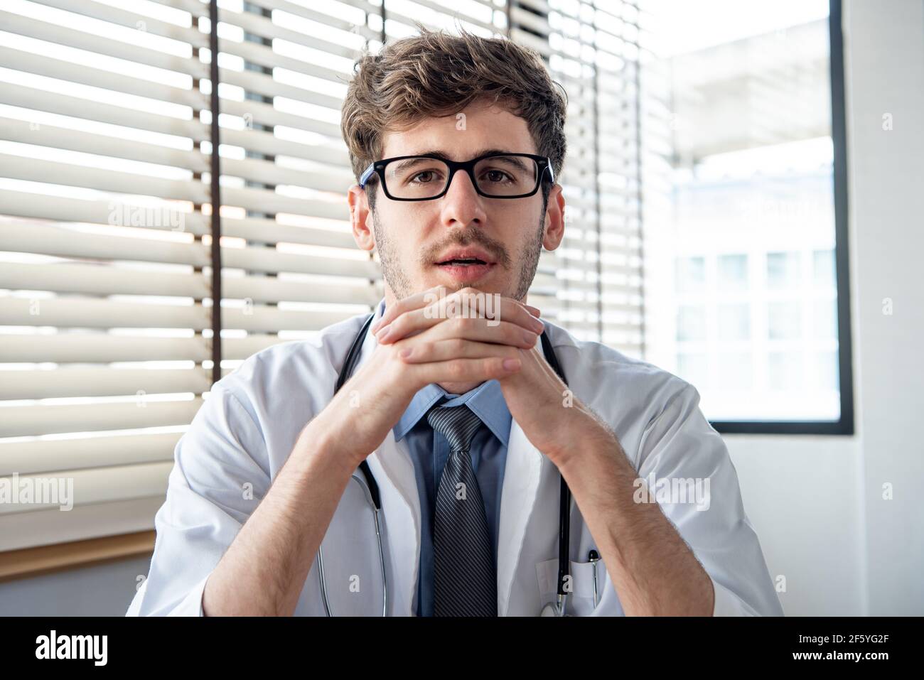 Junge männliche Arzt Blick auf die Kamera während der Herstellung von Video Konferenzschaltung aus dem Krankenhaus anrufen Stockfoto