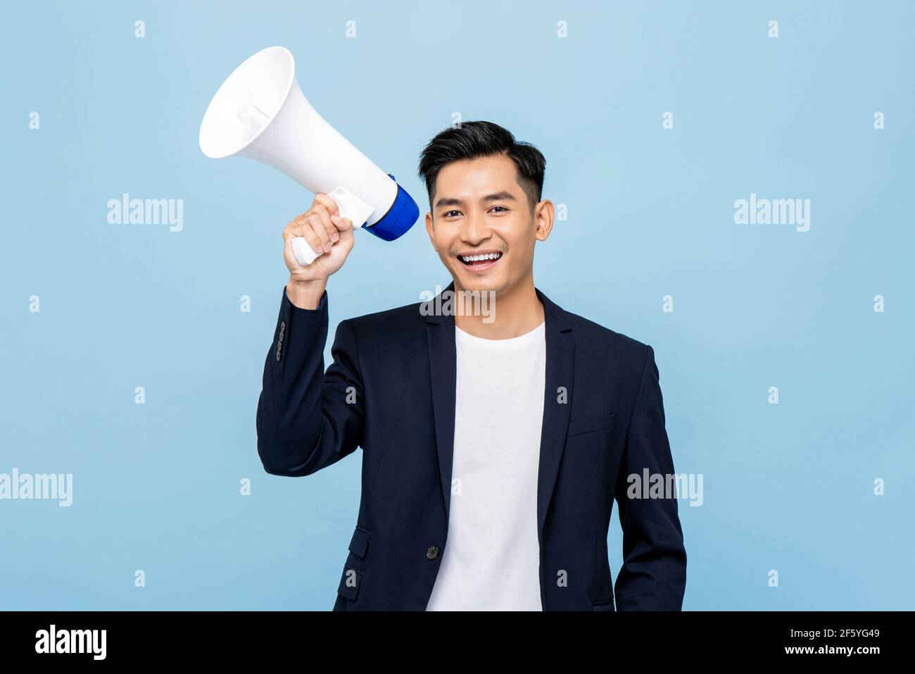 Lächelnd schöner asiatischer Mann hält Megaphon in hellblau isoliert Hintergrund Stockfoto