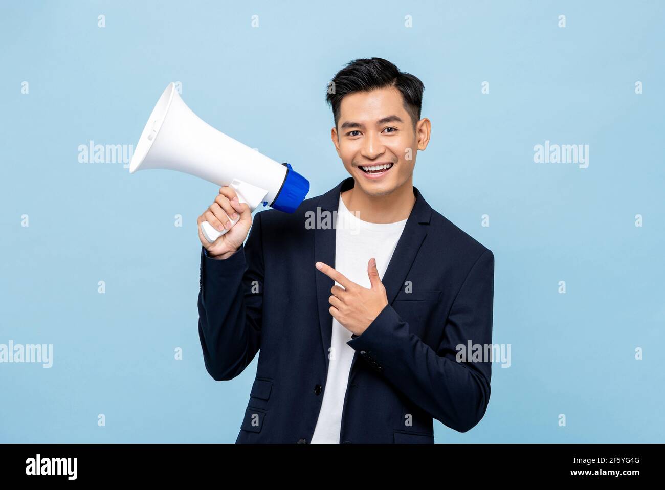 Lächelnd schöner asiatischer Mann hält Megaphon in hellblau isoliert Hintergrund Stockfoto