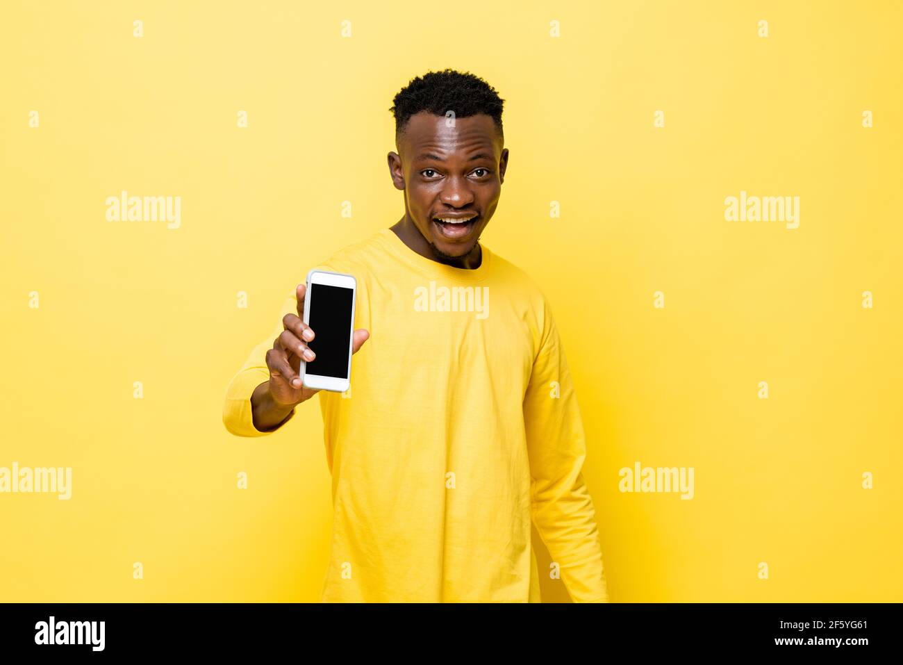 Überrascht junger afrikanischer Mann zeigt Handy in der Hand Auf gelbem isoliertem Studiohintergrund Stockfoto