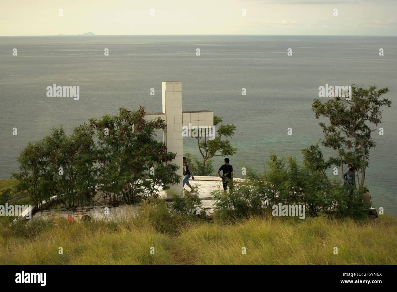 Junge Menschen, die eine Freizeit unter einem großen christlichen Kreuz, das mit Blick auf das Meer gebaut, auf einem Küstenhügel in Kajuwulu in der Nähe von Maumere, Flores Island. Stockfoto