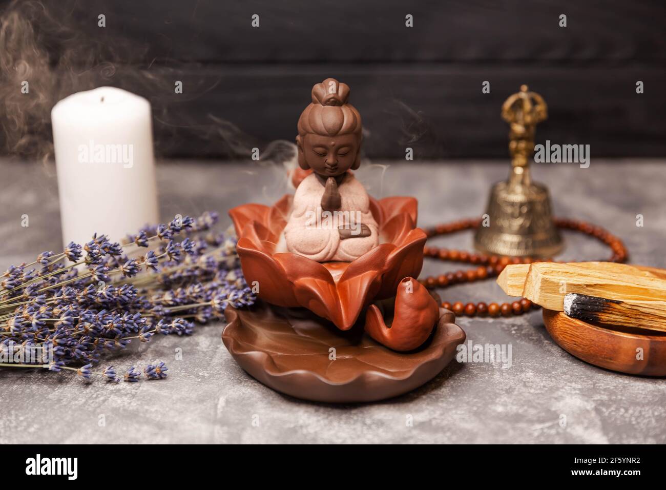 Buddha-Figur und rauchiger Weihrauch mit Glocke und Rosenkranz. Aromatherapie Stockfoto