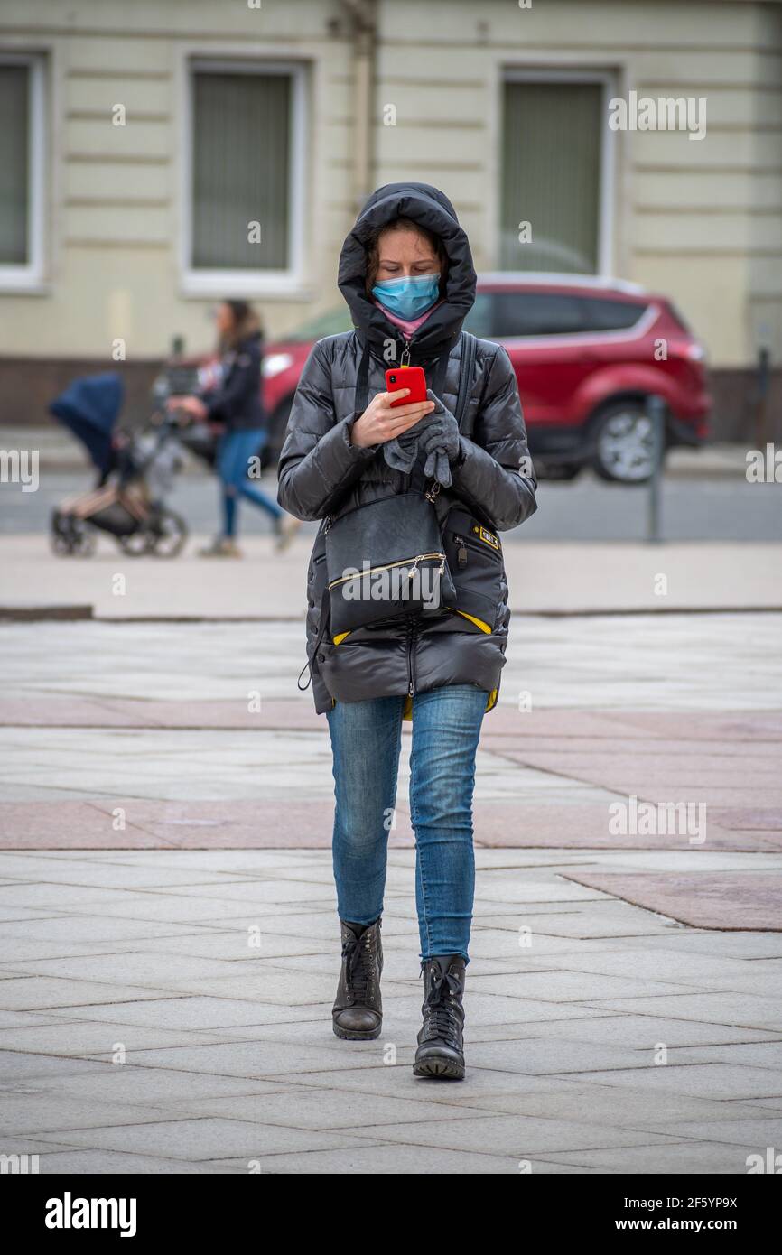 Mädchen oder Frau, die mit Maske und Smartphone auf der Straße während Covid oder Coronavirus Einschränkungen, vertikal Stockfoto