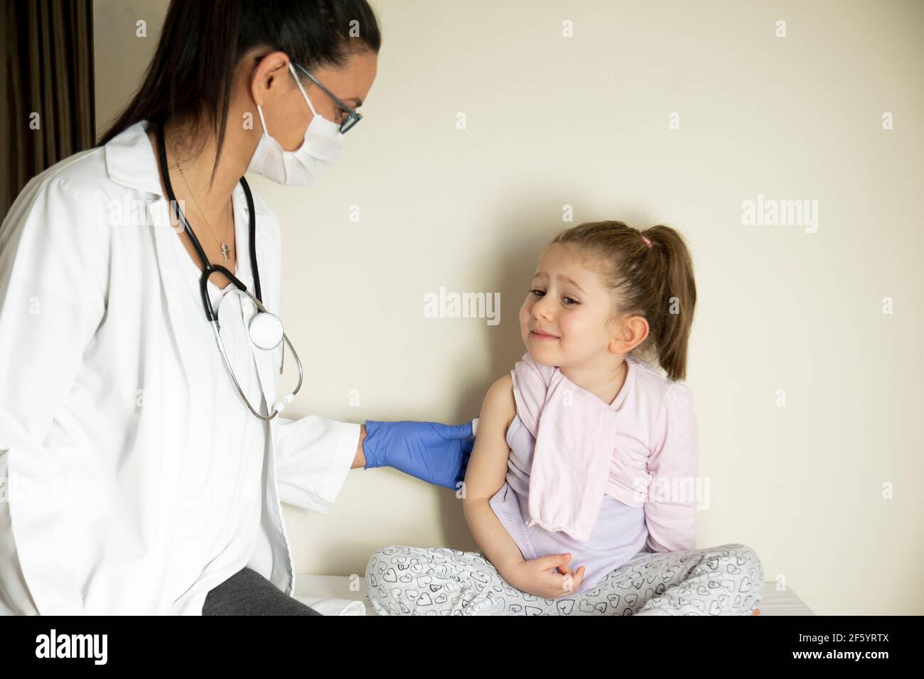 Molliges kleines Mädchen bei der pädiatrischen Untersuchung durch ihren Arzt. Geimpft von ihrem Arzt. Selektiver Fokus. Covid Impfstoff Baby Stockfoto