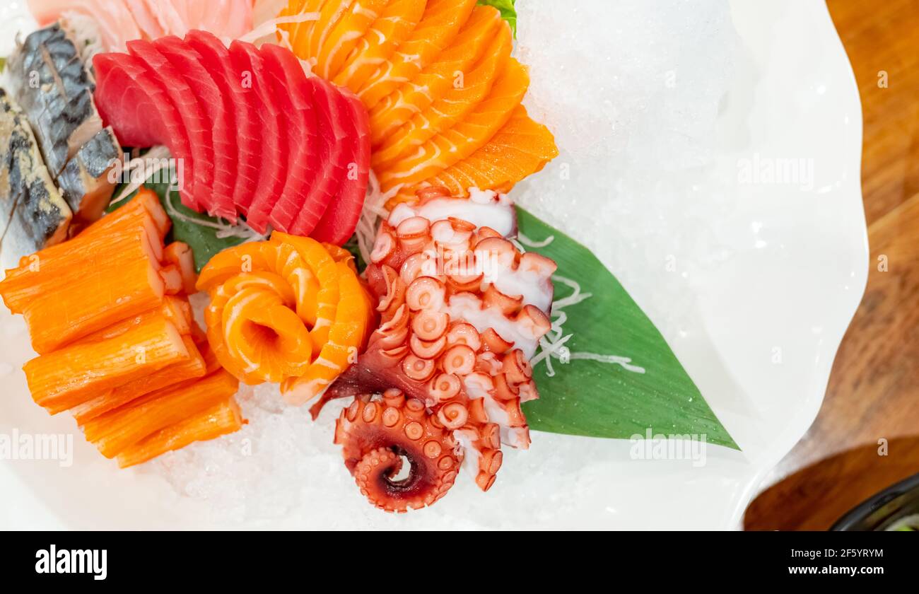 Japanisches Essen Combo Set. Lachs, Thunfisch-Sashimi, Riesenoktopus und Krabbenstäbchen servieren mit zerdrücktem Eis auf weißem Teller auf dem Restauranttisch. Fischfleisch. Stockfoto